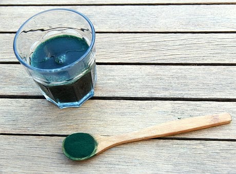 Szklanka z koktajlem ze spiruliny obok drewniana łyżka z proszkiem spiruliny. Superfood zdrowe odżywanie żywienie dieta fit dietetyka